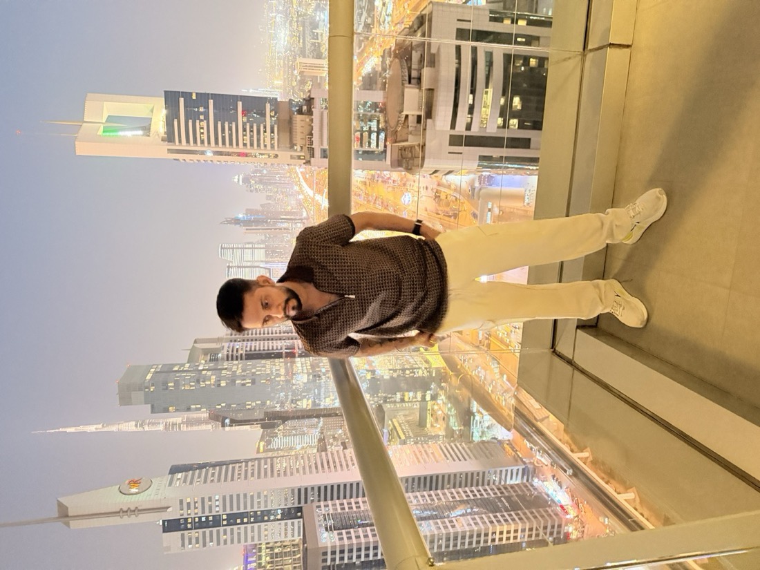 Digital Pratik standing on a glass skywalk at night with the Dubai skyline behind him